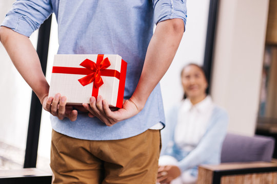 Middle aged husband hiding a surprise gift and roses for surprising his wife on special day such as birthday or wedding anniversary. Celebration and holiday concept