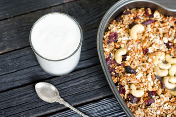 Glass of yogurt and granola with cashews on a baking sheet. Black wooden table