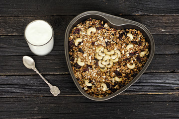 Glass of yogurt and granola with cashews on a baking sheet. Black wooden table