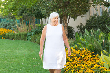 Older lady walking at the garden and admiring the flowers and she wears a white dress