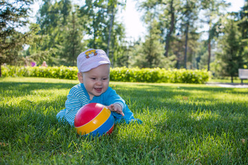 baby sitting on the soft grass in the city Park with his colorful ball