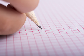 Pencil held by a hand writing on a grid sheet