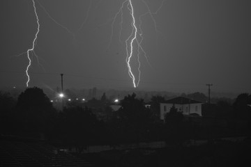 Black and white photo of thunders during a thunderstorm over a small village
