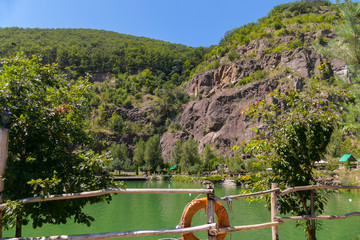 The lake at the foot of a rocky mountain is fenced with a wooden fence. Around a gazebo for rest