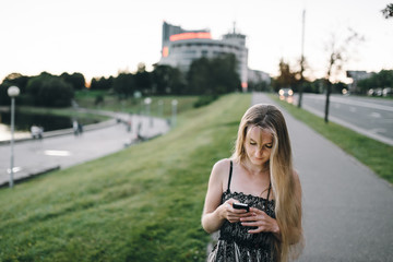 Attractive young girl with long hair in a beautiful outdoor dress with smartphone