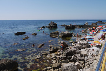 Fototapeta na wymiar Tourists, resting on the beach next to the large stone boulders, going far into the sea