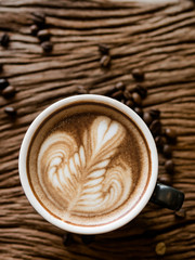 Top view of hot coffee in a cup with beautiful latte art and coffee beans on wooden table background