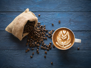 Top view of hot coffee in a cup with beautiful latte art and coffee beans on blue wooden table background