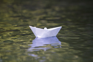 Close-up of simple small white origami paper boat floating quietly in yellow clear river or sea water under bright summer sky. Freedom, dreams and fantasies concept, copyspace background. © bilanol