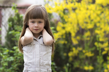Portrait of a pretty little long-haired blond preschool girl in sleeveless white dress smiling...