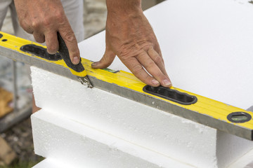 Close-up of worker hand with knife and level cutting white rigid polyurethane foam sheet for house...