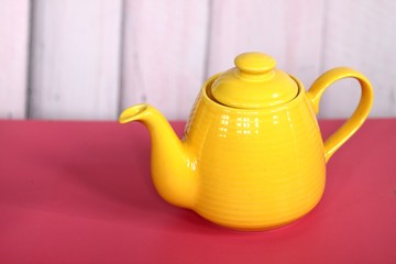 Yellow ceramic teapot on wooden table with pink background.