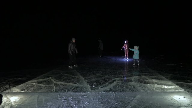 Family is ice skating night. Girls and boys to ride figure ice skates in nature. Mother, father, daughter and son riding together on ice in cracks. Outdoor winter fun for athlete nice winter weather