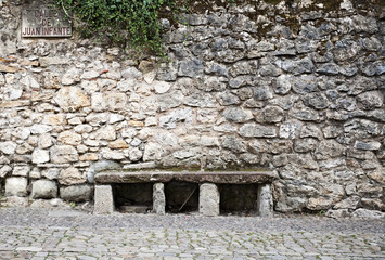 Sitzbank vor einer Natursteinmauer in einer gepflasterten Gasse (Calle de Juan Infante) in...
