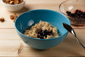 Porridge in a bowl with the berries, walnuts and cocoa on bright wooden table. Healthy breakfast image. Copy space