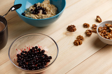 Porridge in a bowl with the berries, walnuts on bright wooden table. Healthy breakfast image. Copy space