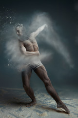 Fototapeta na wymiar Dancing in flour concept. Muscle fitness guy man male dancer in dust / fog. Guy wearing white shorts making dance element in flour cloud on isolated grey / black background