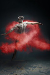 Dancing in flour concept. Muscle fitness guy man male dancer in red dust / fog. Guy wearing white shorts making dance element in flour cloud on isolated grey background. HIV / AIDS red ribbon concept. - obrazy, fototapety, plakaty