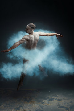 Dancing in flour concept. Muscle fitness guy man male dancer in light blue dust / fog. Guy making dance element in flour cloud. Light blue ribbon as a symbol of prostate cancer concept.