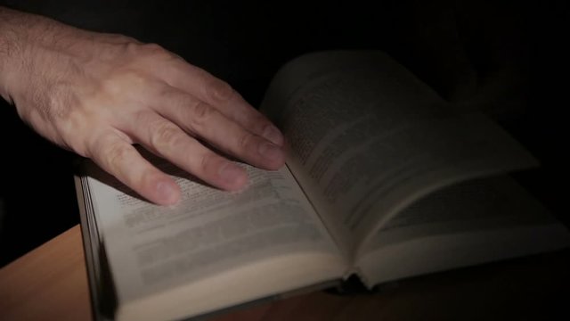 Close-up of a man's hand holding an open paper book, turning the pages with his fingers