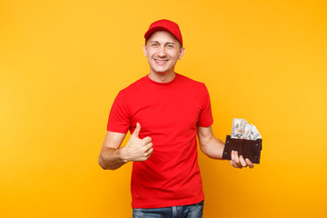 Delivery man in red uniform isolated on yellow orange background. Professional male employee in cap, t-shirt courier or dealer holding bundle lots of dollars, cash money. Service concept. Copy space.