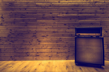 Guitar amplifier on wooden wall and floor, music studio - obrazy, fototapety, plakaty
