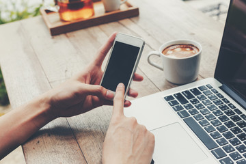 Business man holding phone and using laptop on wooden table. Vintage toned.
