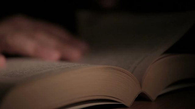 Close-up of a man's hand holding an open paper book, turning the pages with his fingers