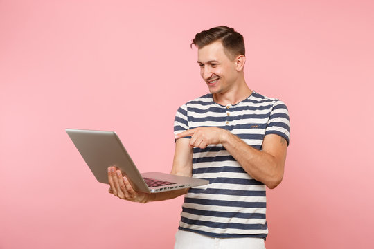 Portrait of handsome young man wearing striped t-shirt working on laptop computer, copy space isolated on trending pastel pink background. People sincere emotions lifestyle concept. Advertising area.