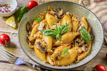 Pasta Conchiglioni with mushrooms in a vintage bowl on concrete background.