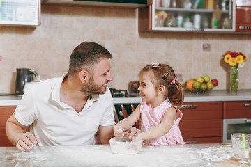 Fototapeta na wymiar Little kid girl helps man to cook Christmas ginger cookies, playing with flour at table. Happy family dad, child daughter cooking food in weekend morning. Father's day holiday. Parenthood, childhood.