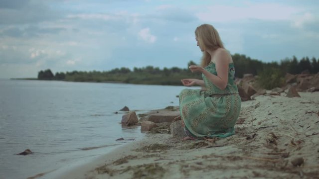 Carefree redhead woman in summer dress collecting sea stones and shells on the beach. Joyful ginger females picking up pebbles while spending great time at seaside during summer vacations.