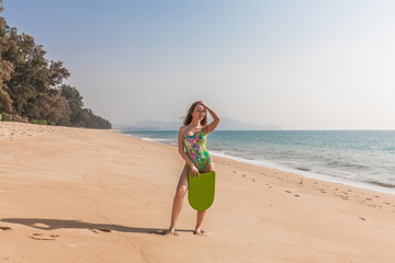 Beautiful woman with board stands near the sea with green board. Phuket, Thailand