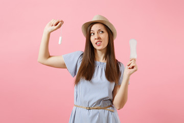 Portrait of young woman in blue dress holding sanitary napkin, tampon for variant safety menstruation days isolated on pink background. Medical healthcare, gynecological, choice concept. Copy space.