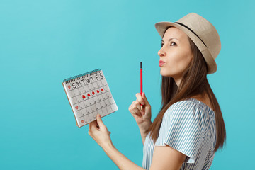 Portrait pensive woman in blue dress, hat holding red pencil, female periods calendar for checking...