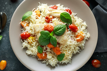 Steamed cod fish with rice and cherry mix tomatoes and basil herbs in a plate