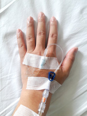 Patient hand with the tube of normal saline infusion on white cloth background