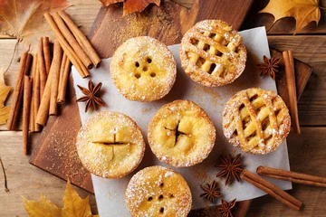 Zelfklevend Fotobehang Set of different mini apple pies decorated sugar powder and cinnamon on wooden table top view. Autumn pastry dessert. © juliasudnitskaya