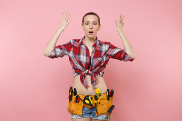 Confused shocked handyman woman in shirt denim shorts, kit tools belt full of variety useful instruments spreading hands isolated on pink background. Female doing male work. Renovation problem concept