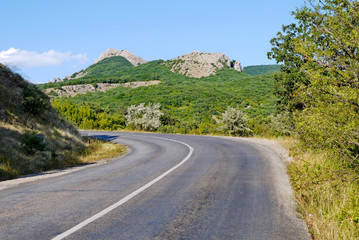 the road is rolled up against the background of high cliffs covered with grass under the blue sky