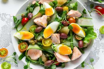 Healthy Nicoise salad with salmon, colourful sweet cherry tomatoes, olives, green beans, cucumber ribbons, soft boiled eggs, water-cress leaves with Mediterranean seasoning