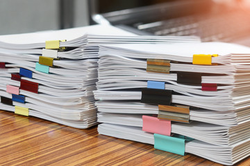 Close up pile of unfinished paperwork separated by colorful binder clips on office desk waiting to be managed. Stack of homework assignments. Report papers stacks. Business and education concept.