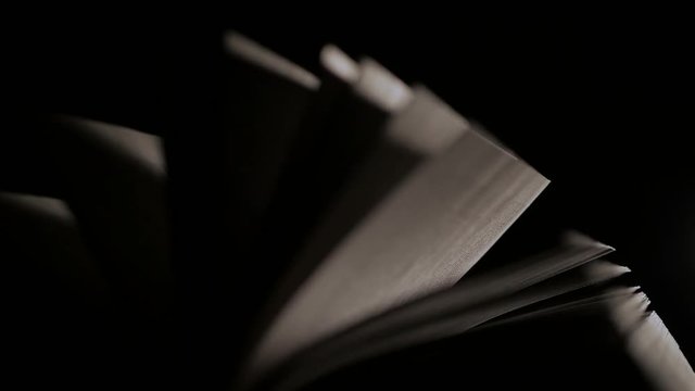 Close-up of an open book at night in a ray of light. Pages are heard from the wind
