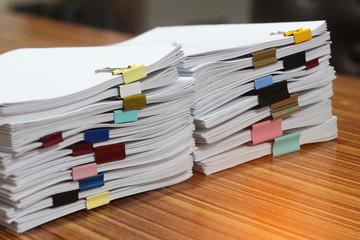 Close up pile of unfinished paperwork separated by colorful binder clips on office desk waiting to be managed. Stack of homework assignments. Report papers stacks. Business and education concept.