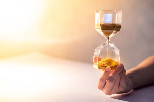 Close up of gold sand running through the shape of modern hourglass on male hand.Time passing and running out of time. Urgency countdown timer for business deadline concept with copy space