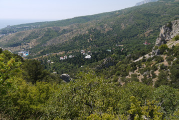 A small cozy village surrounded by forest covered with mountains on the background of a wide Black Sea