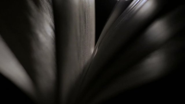 Close-up of an open book at night in a ray of light. Pages are heard from the wind