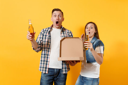 Young amazed surprised couple woman and man sport fans cheer up support team holding beer bottle and italian pizza in cardboard flatbox isolated on yellow background. Sport family leisure lifestyle.