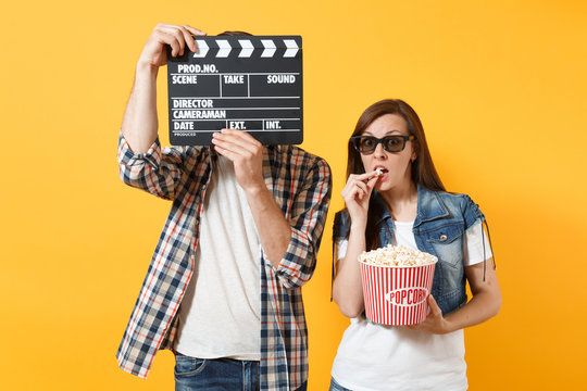 Young Couple Woman Man In 3d Glasses Watching Movie Film On Date Covering Face With Classic Black Film Making Clapperboard Eating Popcorn From Bucket Isolated On Yellow Background. Emotions In Cinema.