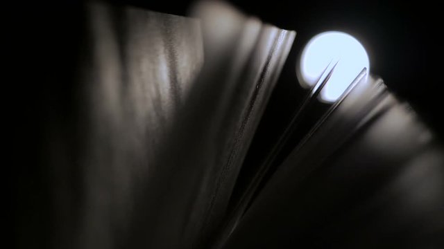 Close-up of an open book at night in a ray of light. Pages are heard from the wind